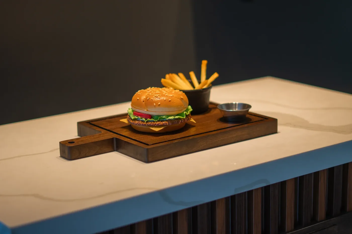 Hamburguesa y papas montadas sobre una tabla de servicio de madera con salsera